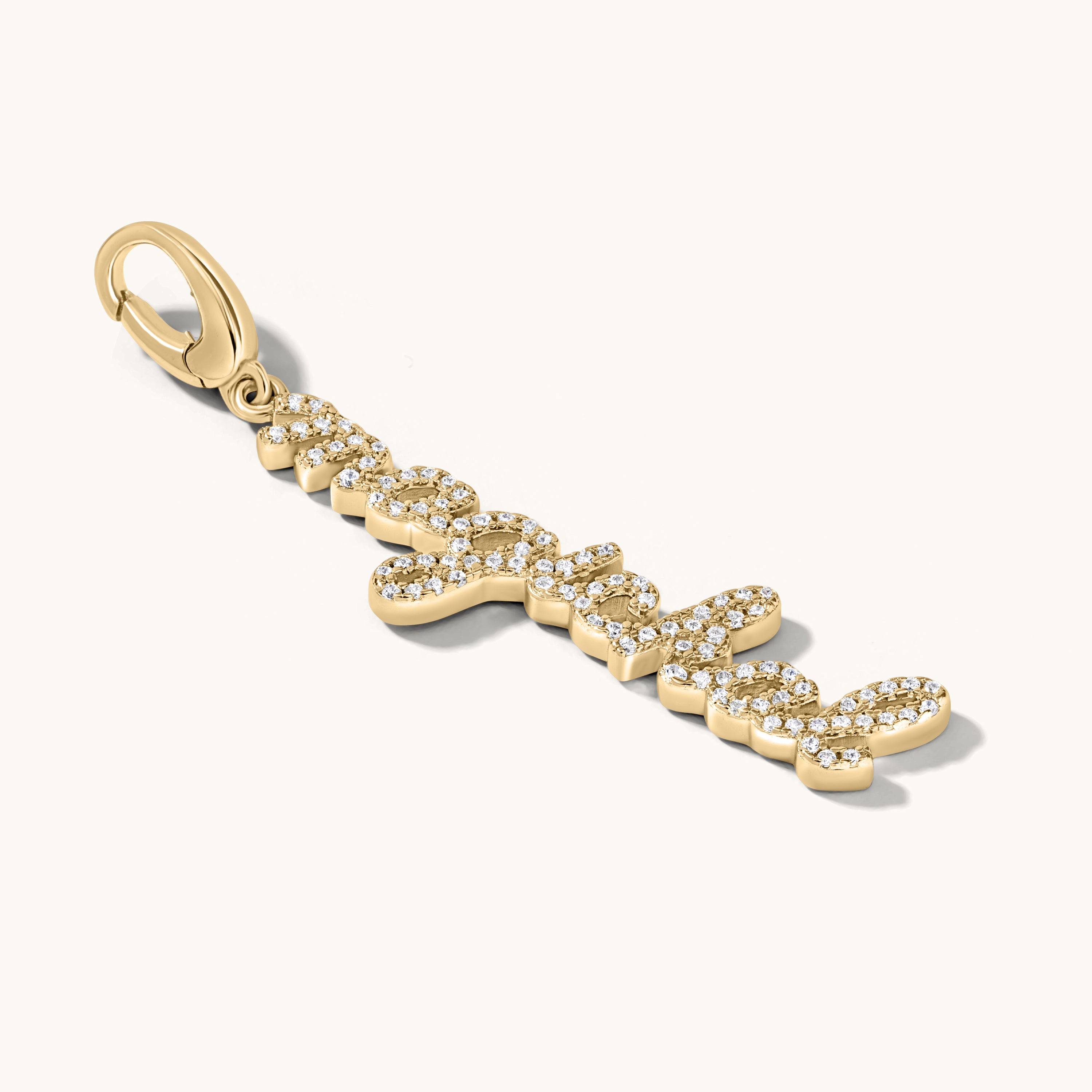 The word magickal is written in elegant cursive script and studded with white topaz stones. It is set in a gold charm pendant against an light cream background.