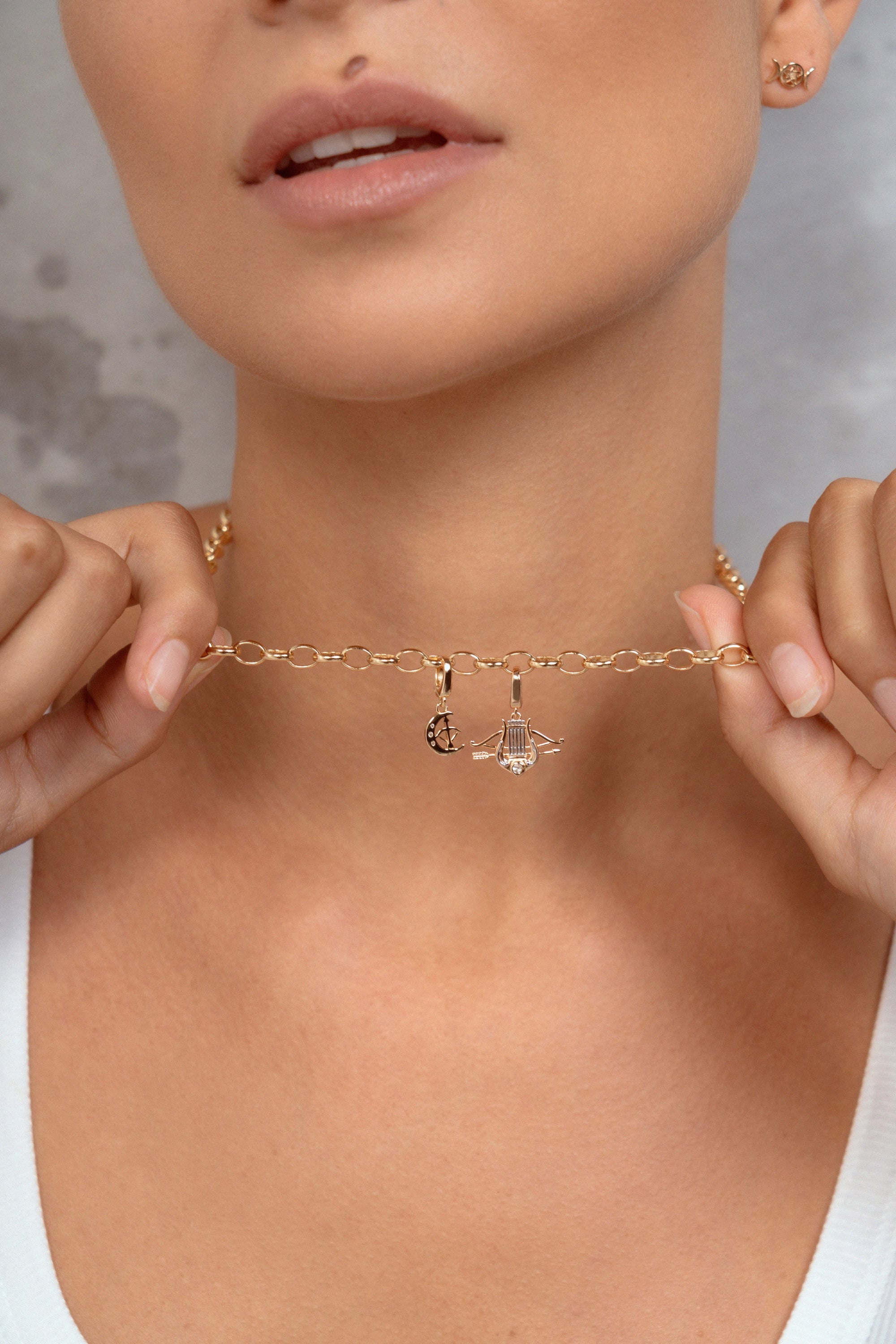 A close-up lifestyle shot of a model wearing a delicate gold chain necklace with two small charms, holding the chain out with both hands to show its scale.