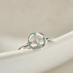 Silver ring with green gemstones on a beige surface