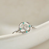 Silver ring with green gemstones on a beige surface