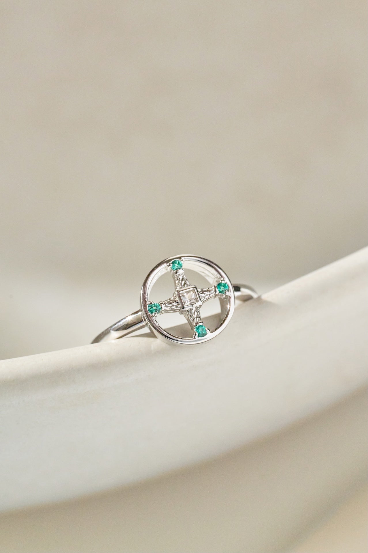 Silver ring with green gemstones on a beige surface