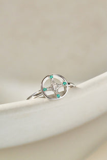 Silver ring with green gemstones on a beige surface