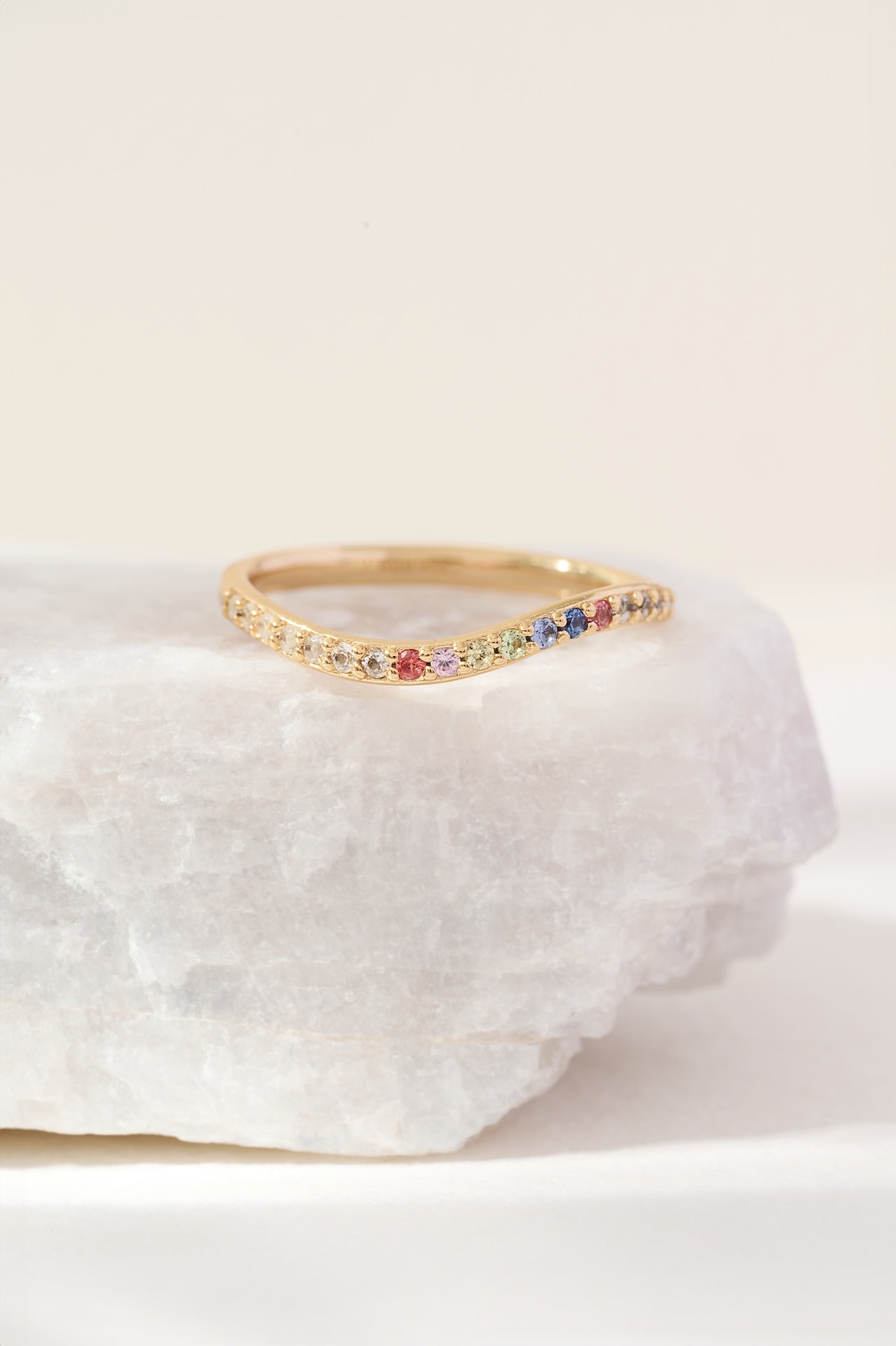 Gold ring with colorful stones on a white stone surface