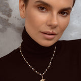 A close-up of a woman wearing a delicate gold chain necklace with small white pearls and a small gold pendant, paired with a black turtleneck sweater.