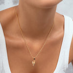 A close-up of a model wearing a delicate gold chain necklace with a small pendant, styled with a white ribbed tank top.