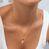 A close-up of a model wearing a delicate gold chain necklace with a small pendant, styled with a white ribbed tank top.