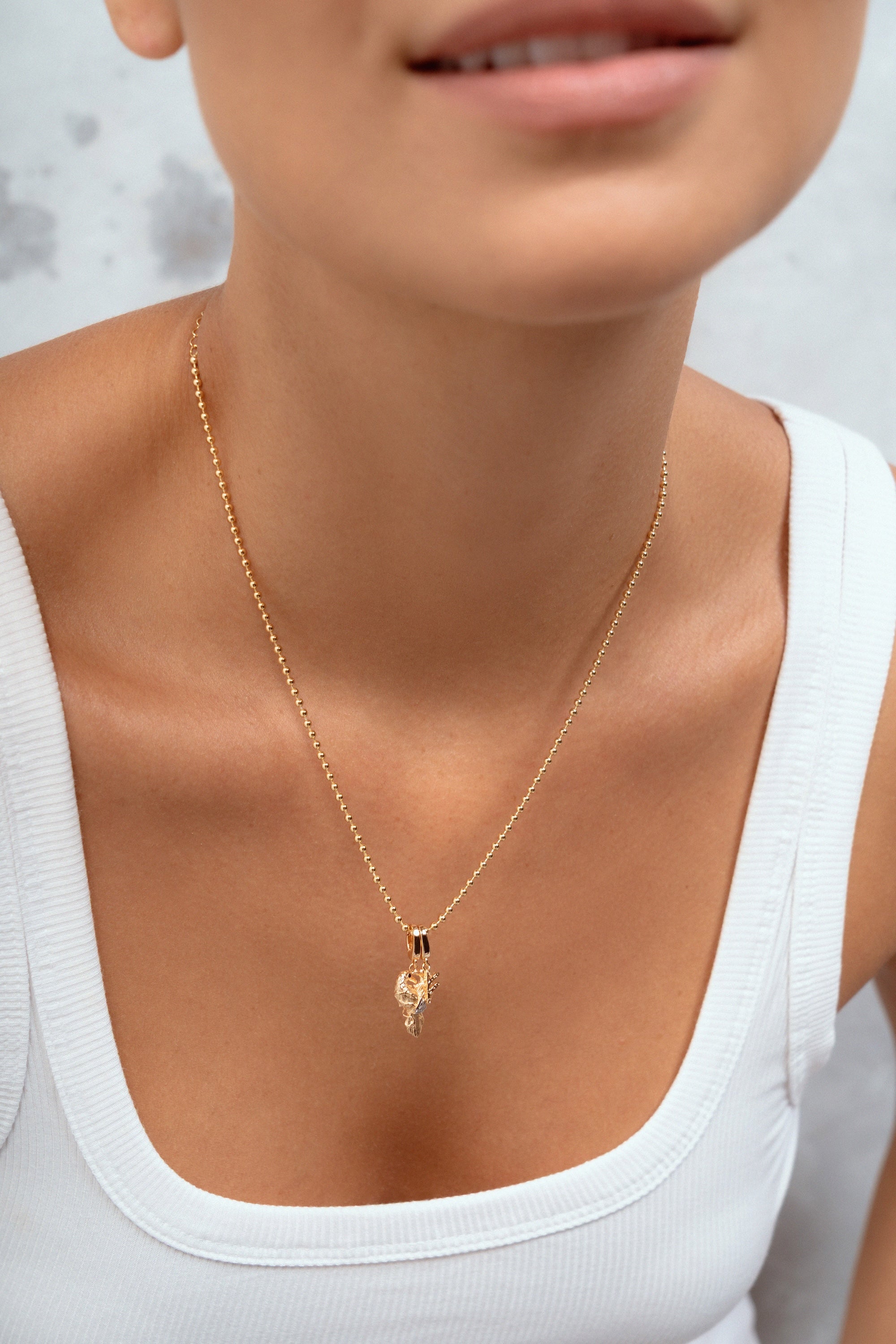 A close-up of a model wearing a delicate gold chain necklace with a small pendant, styled with a white ribbed tank top.