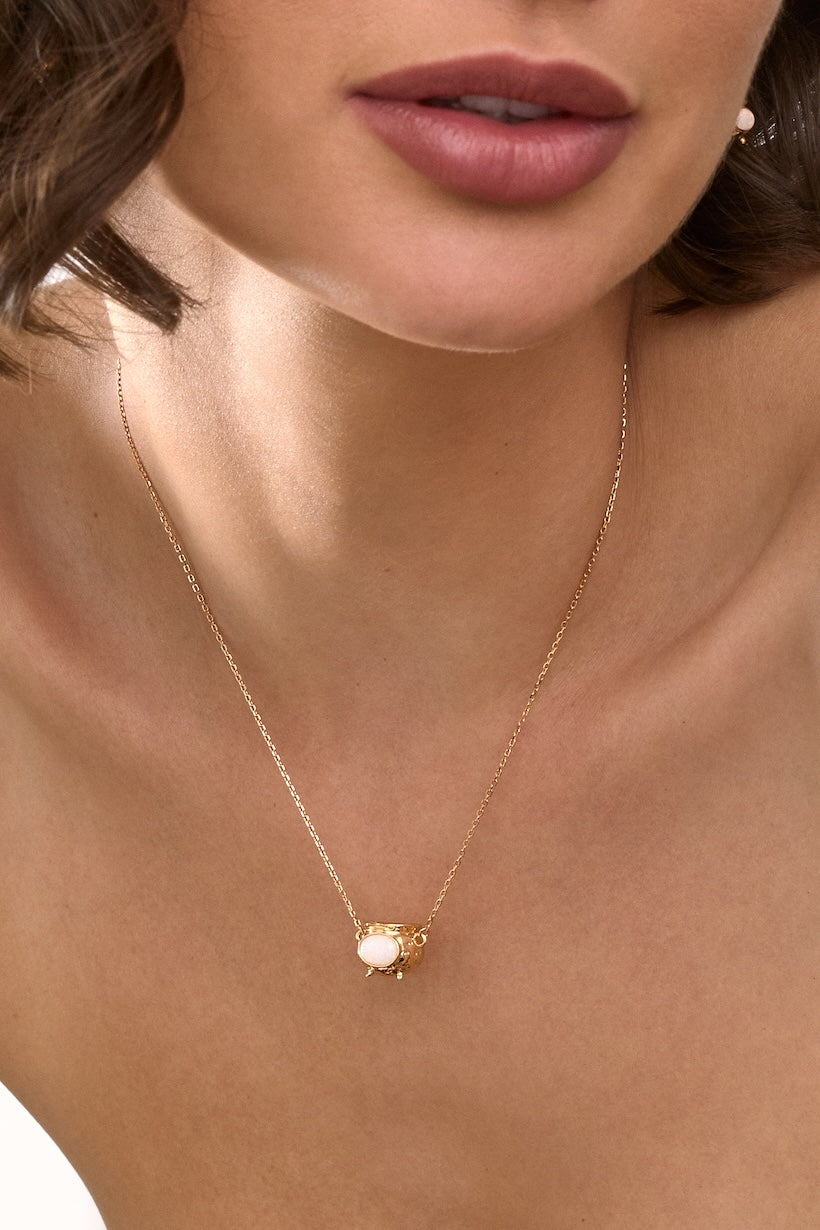 Close-up of a gold necklace with a Cauldron pendant on a person's neck.