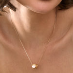 Close-up of a gold necklace with a Cauldron pendant on a person's neck.