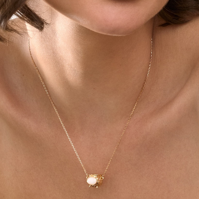 Close-up of a gold necklace with a Cauldron pendant on a person's neck.