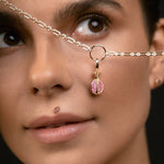 A close-up of a model wearing a delicate gold chain necklace with a small gold ring and a dangling pink and gold bead charm.
