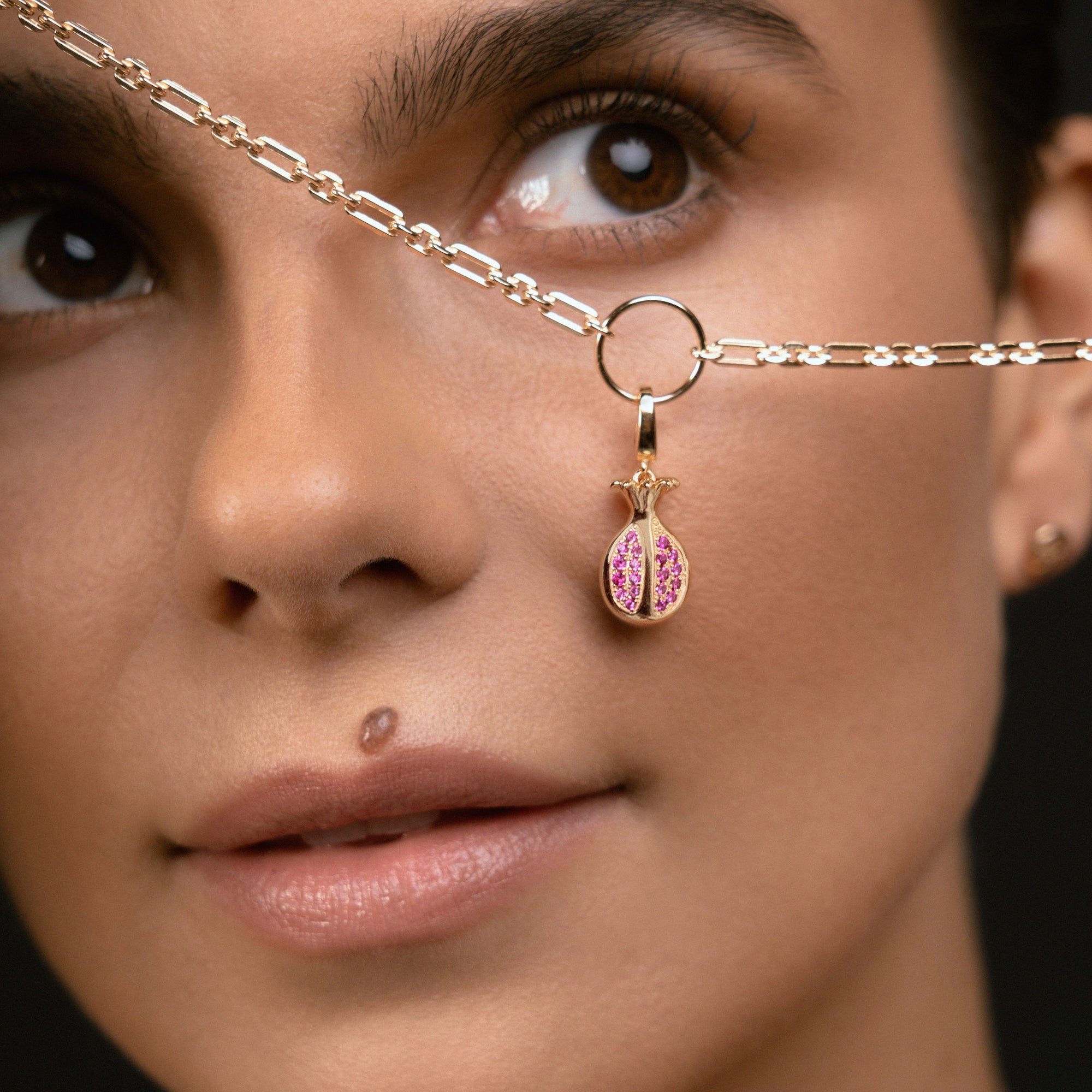 A close-up of a model wearing a delicate gold chain necklace with a small gold ring and a dangling pink and gold bead charm.
