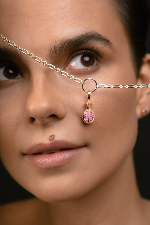 A close-up of a model wearing a delicate gold chain necklace with a small gold ring and a dangling pink and gold bead charm.