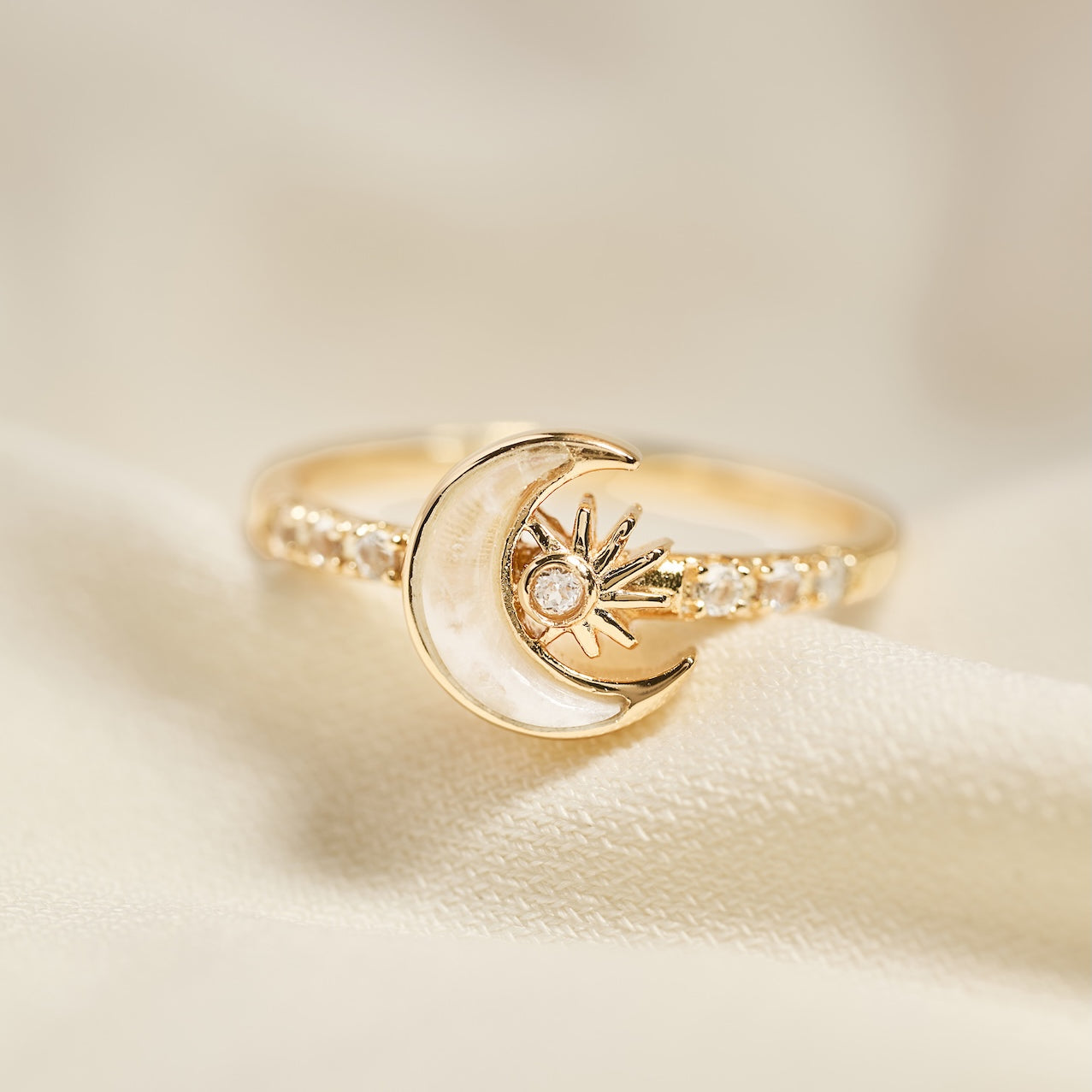 Gold ring with moon and star design on a beige background