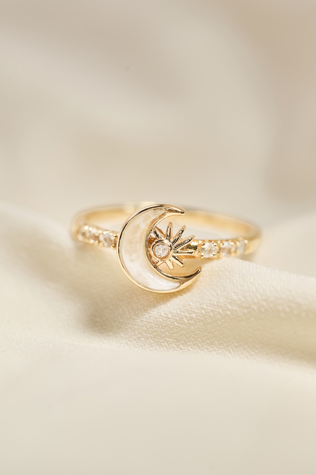 Gold ring with moon and star design on a beige background