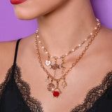 Close-up of a woman wearing a gold necklace with charms against a purple background