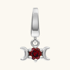 A silver triple moon pendant charm featuring a central faceted red gemstone, set against a plain off-white background.