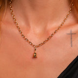 A close-up of a model's neck and chest wearing a gold chain necklace with a small pendant featuring a white-topaz gemstone.