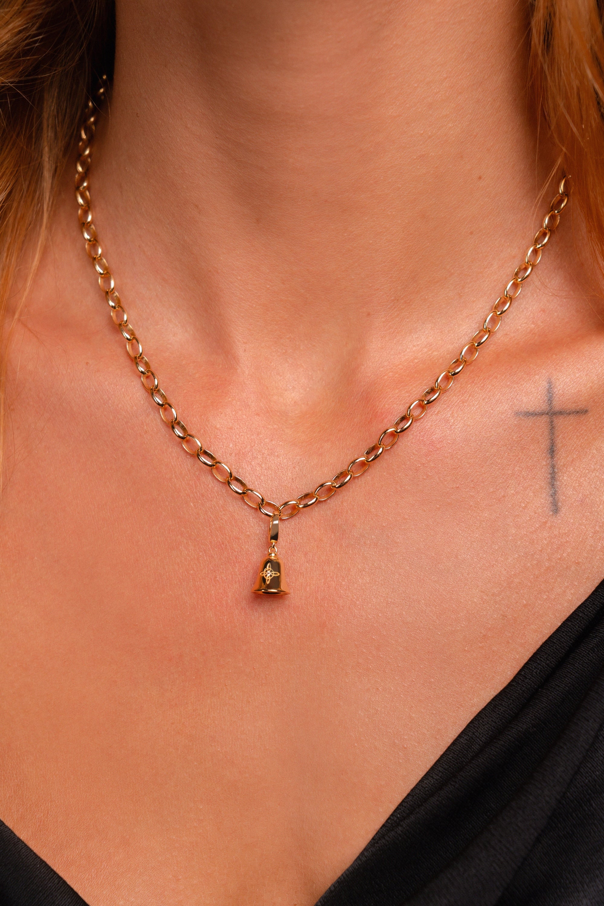 A close-up of a model's neck and chest wearing a gold chain necklace with a small pendant featuring a white-topaz gemstone.