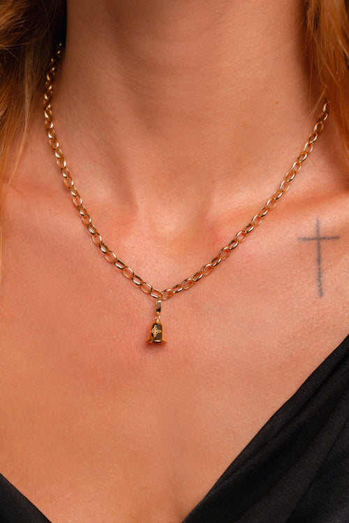 A close-up of a model's neck and chest wearing a gold chain necklace with a small pendant featuring a white-topaz gemstone.