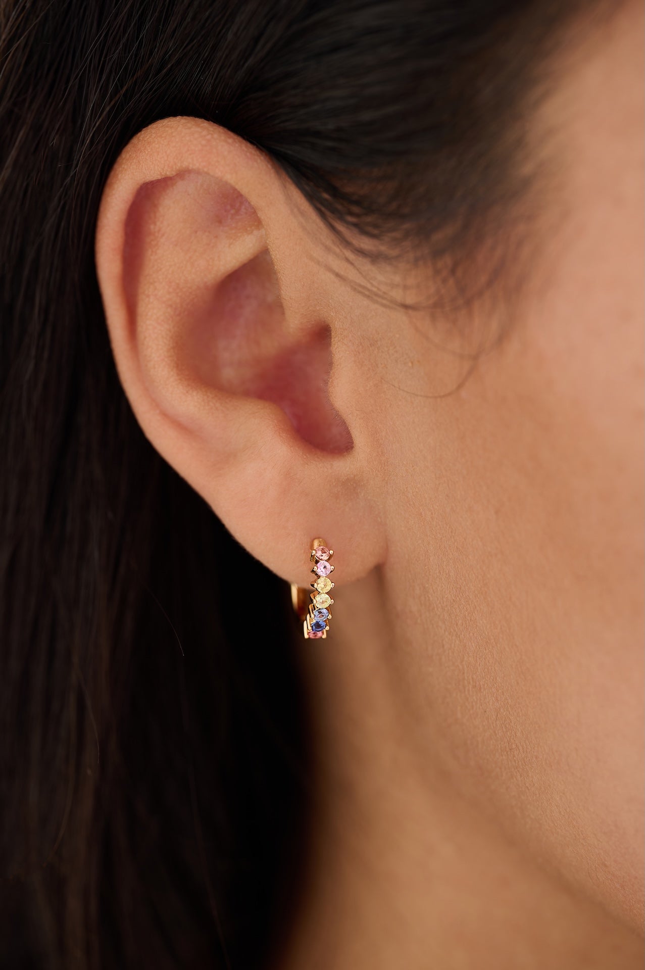 Close-up of an ear wearing a small earring with multicolored stones.