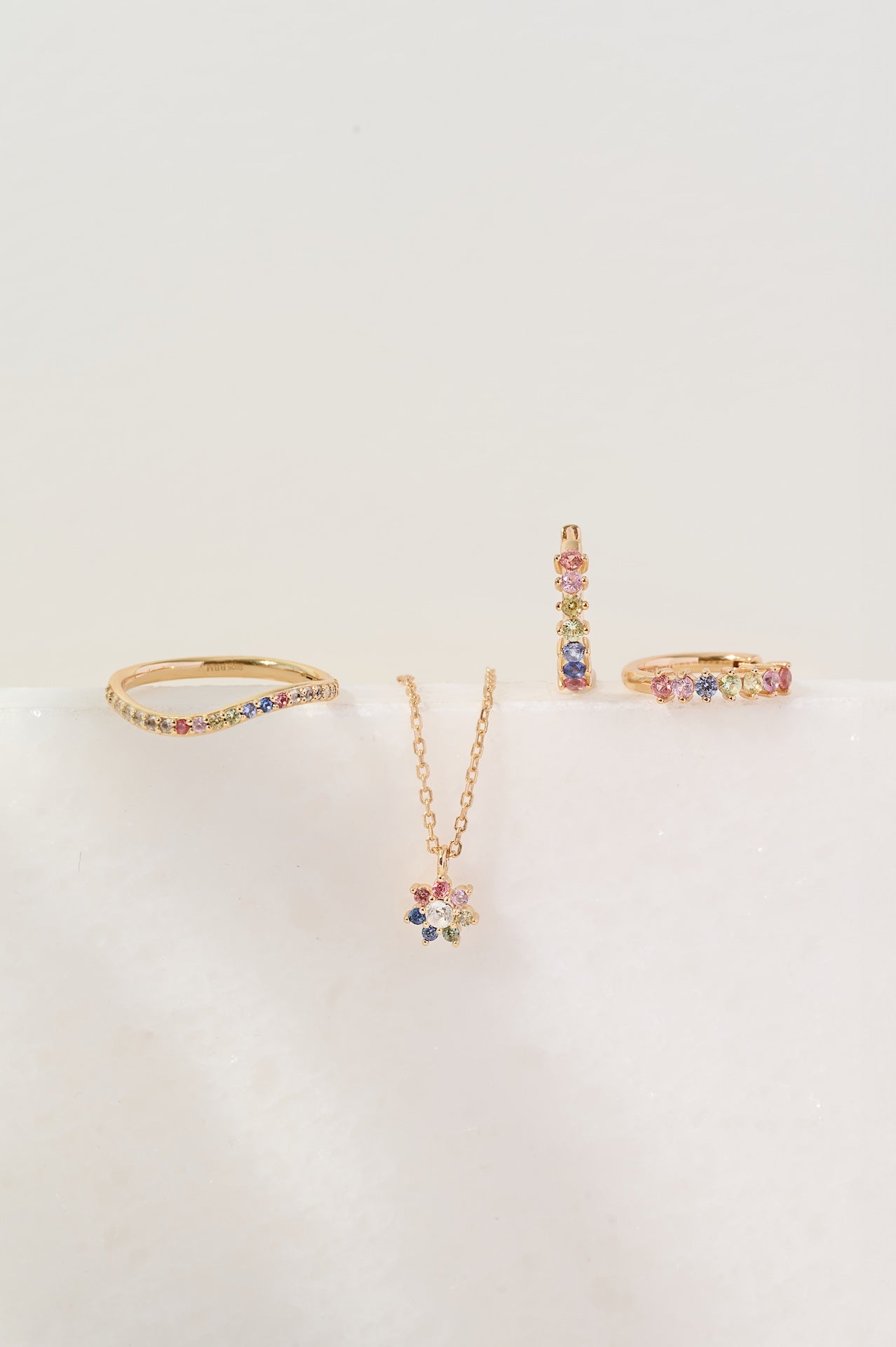 Set of gold jewelry with colorful stones on a light beige background