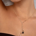 A close-up of a model wearing a delicate gold Y-necklace with a small black oval stone and a tiny white charm.