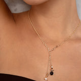 A close-up of a model wearing a delicate gold Y-necklace with a small black oval stone and a tiny white charm.
