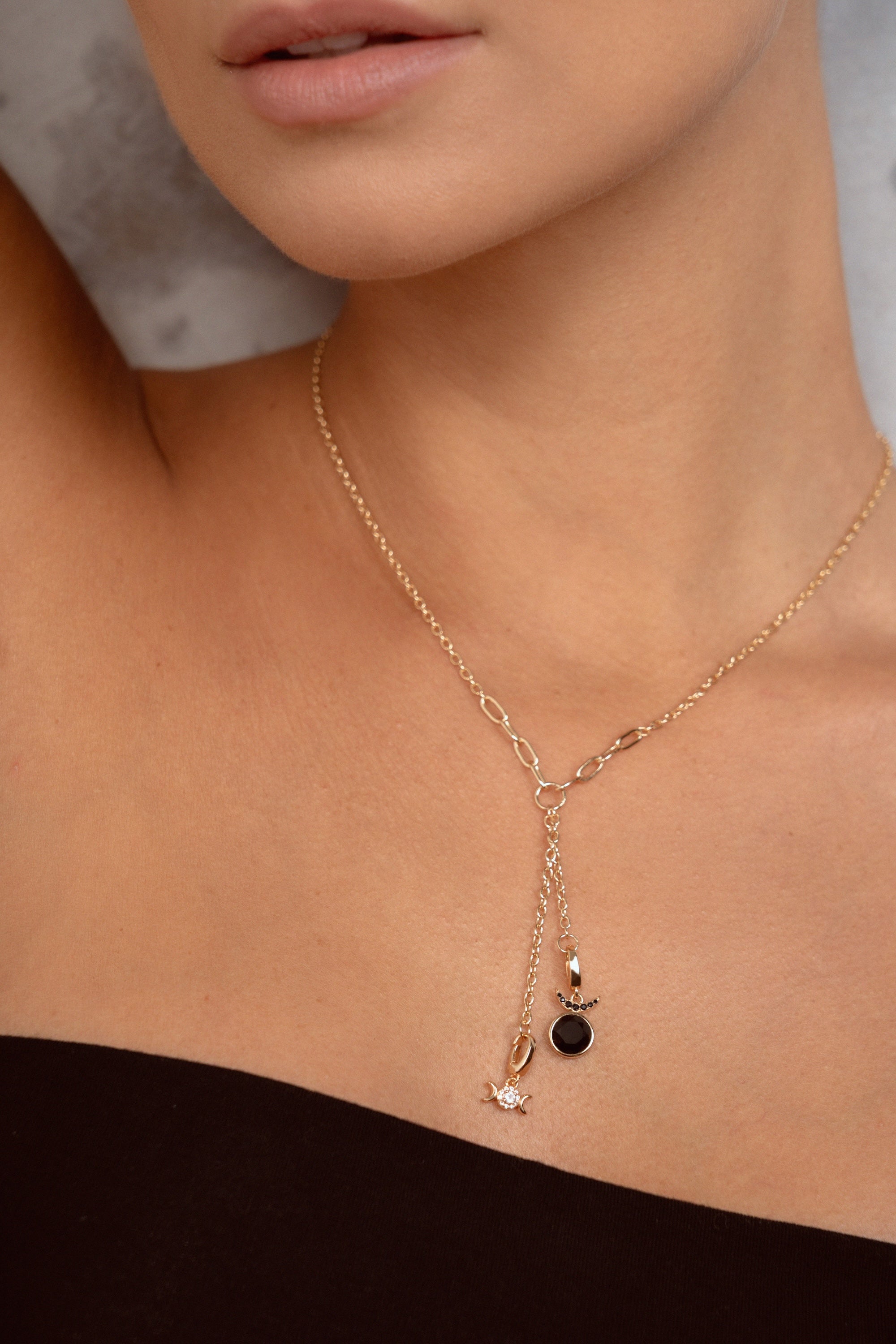 A close-up of a model wearing a delicate gold Y-necklace with a small black oval stone and a tiny white charm.