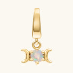 A gold pendant charm featuring a triple moon symbol surrounding a round iridescent white opal gemstone, shown on a light cream background.