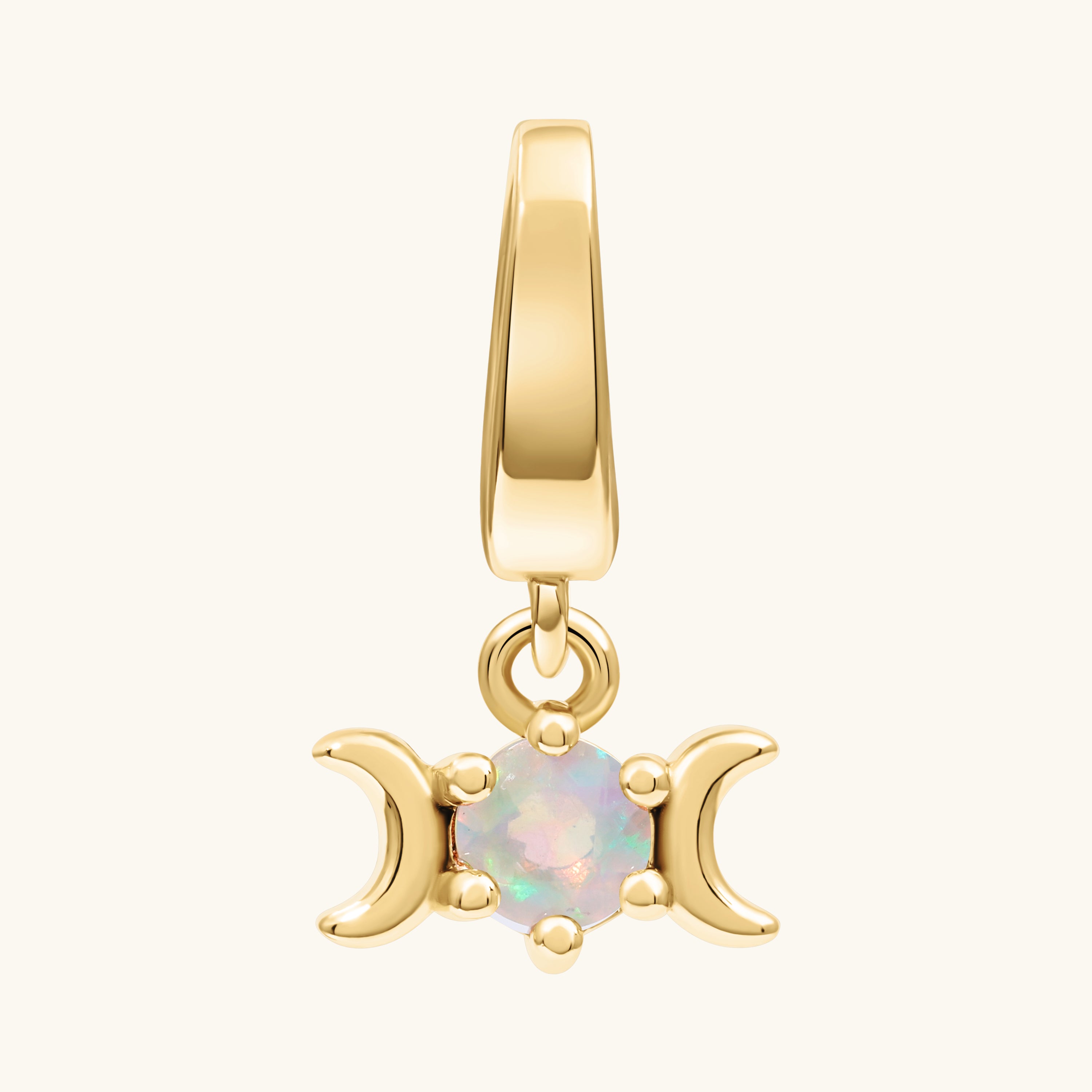 A gold pendant charm featuring a triple moon symbol surrounding a round iridescent white opal gemstone, shown on a light cream background.