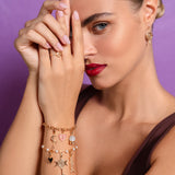 Woman wearing multiple bracelets with charms on a purple background