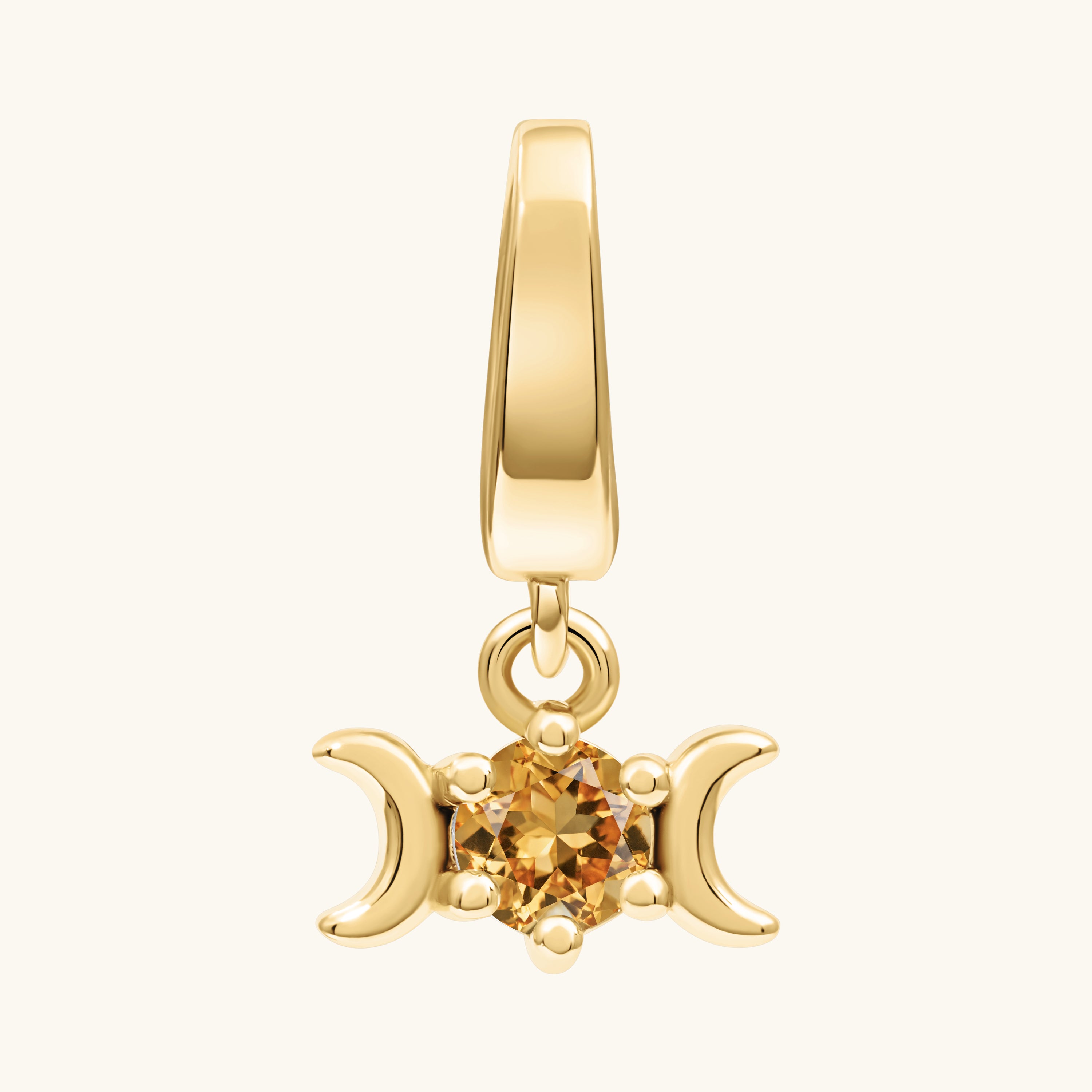 A gold pendant charm featuring a triple moon symbol surrounding a round iridescent yellow citrine gemstone, shown on a light cream background.