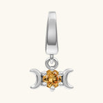A silver triple moon pendant charm featuring a central round-cut orange gemstone, set against a plain off-white background.