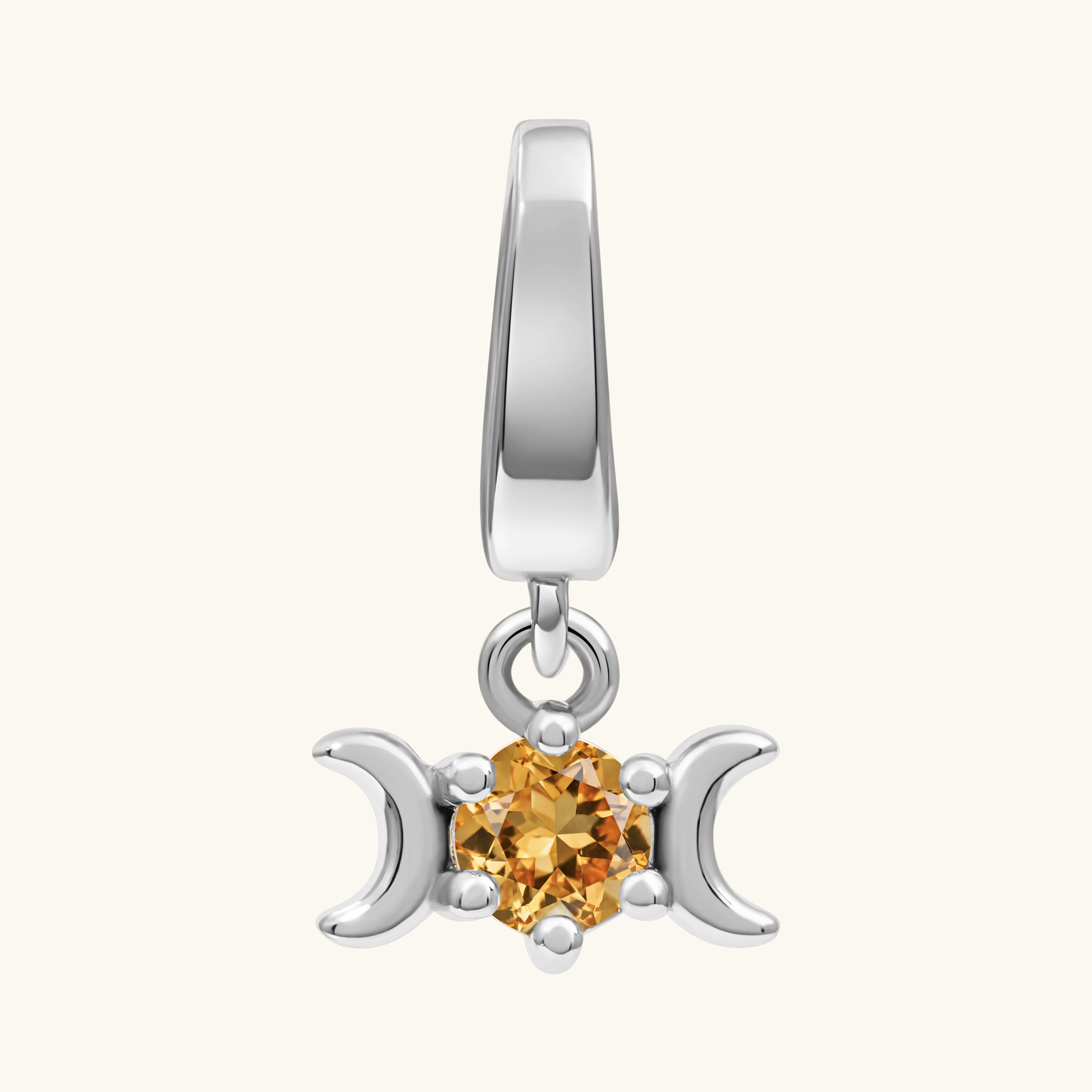 A silver triple moon pendant charm featuring a central round-cut orange gemstone, set against a plain off-white background.