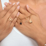 A close-up lifestyle shot of a person wearing a delicate gold charm bracelet with a  three gold pendants, along with a matching gold ring and pearl bracelet.