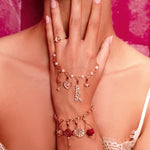 Close-up of a woman's hand wearing multiple gold bracelets with charms against a pink background