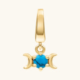 A gold triple moon charm pendant featuring a central turquoise blue stone, set against a plain off-white background.