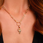 A close-up of a woman’s neck wearing the Preorder: Odin Charm (Ships end October 2026), a gold chain Valknut necklace with a circular pendant and crystal-studded owl inspired by Norse mythology.