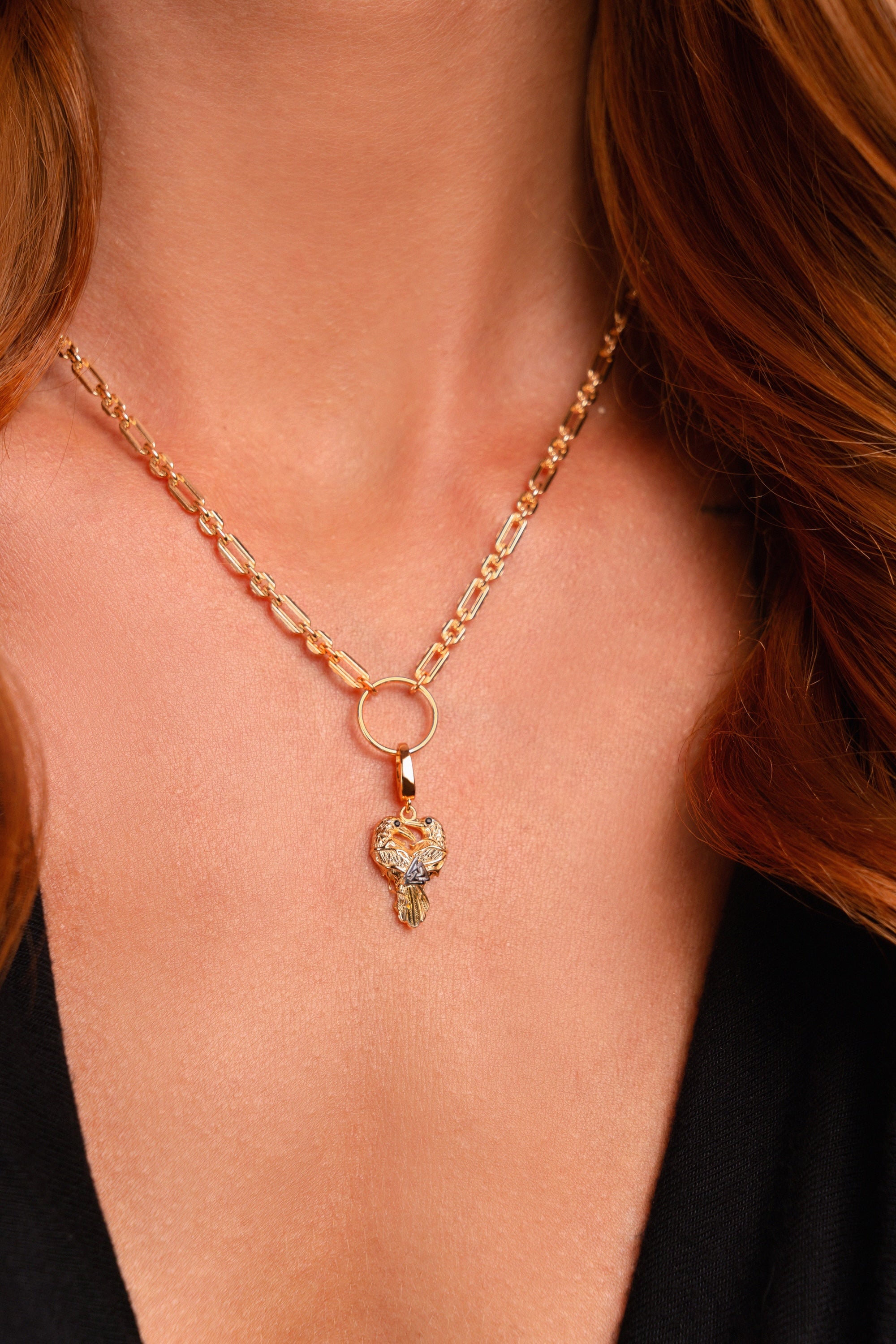 A close-up of a woman’s neck wearing the Preorder: Odin Charm (Ships end October 2026), a gold chain Valknut necklace with a circular pendant and crystal-studded owl inspired by Norse mythology.