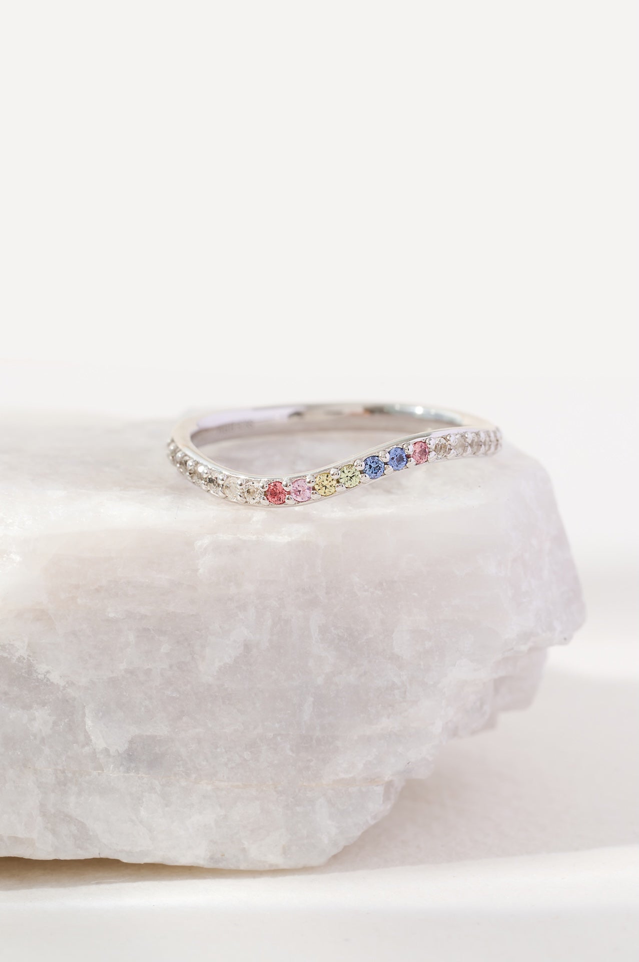Silver ring with colorful gemstones on a white stone surface