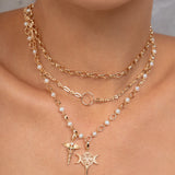 A close-up of a model wearing a layered gold necklace set with white pearl accents and two distinct pendants: a  key, and a caduceus symbol.