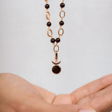 A delicate necklace with a gold chain featuring alternating dark black beads and oval links, hanging above an open hand against a light gray background.