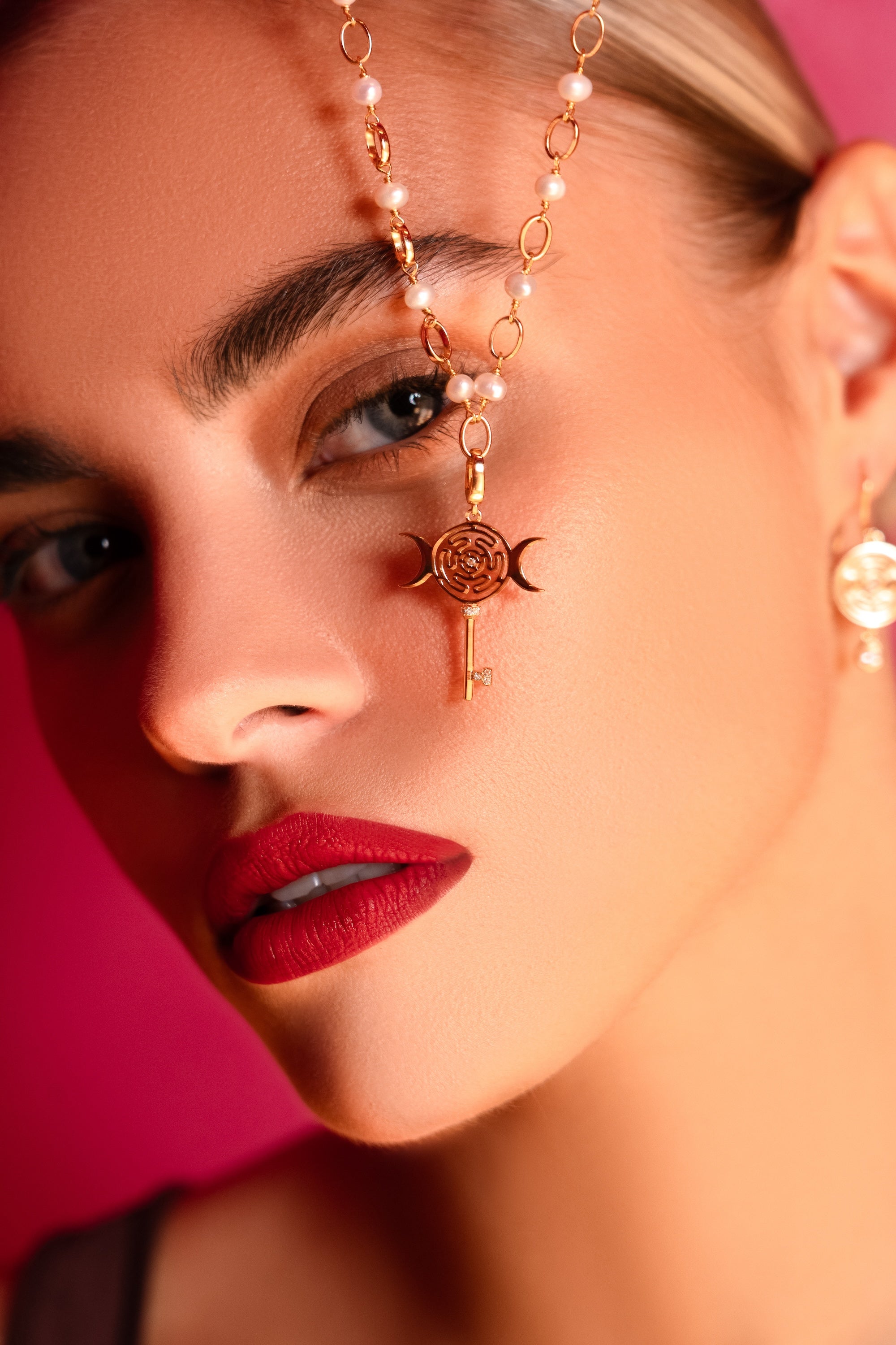 Close-up of a woman holding up a gold necklace ith a key design against a pink background