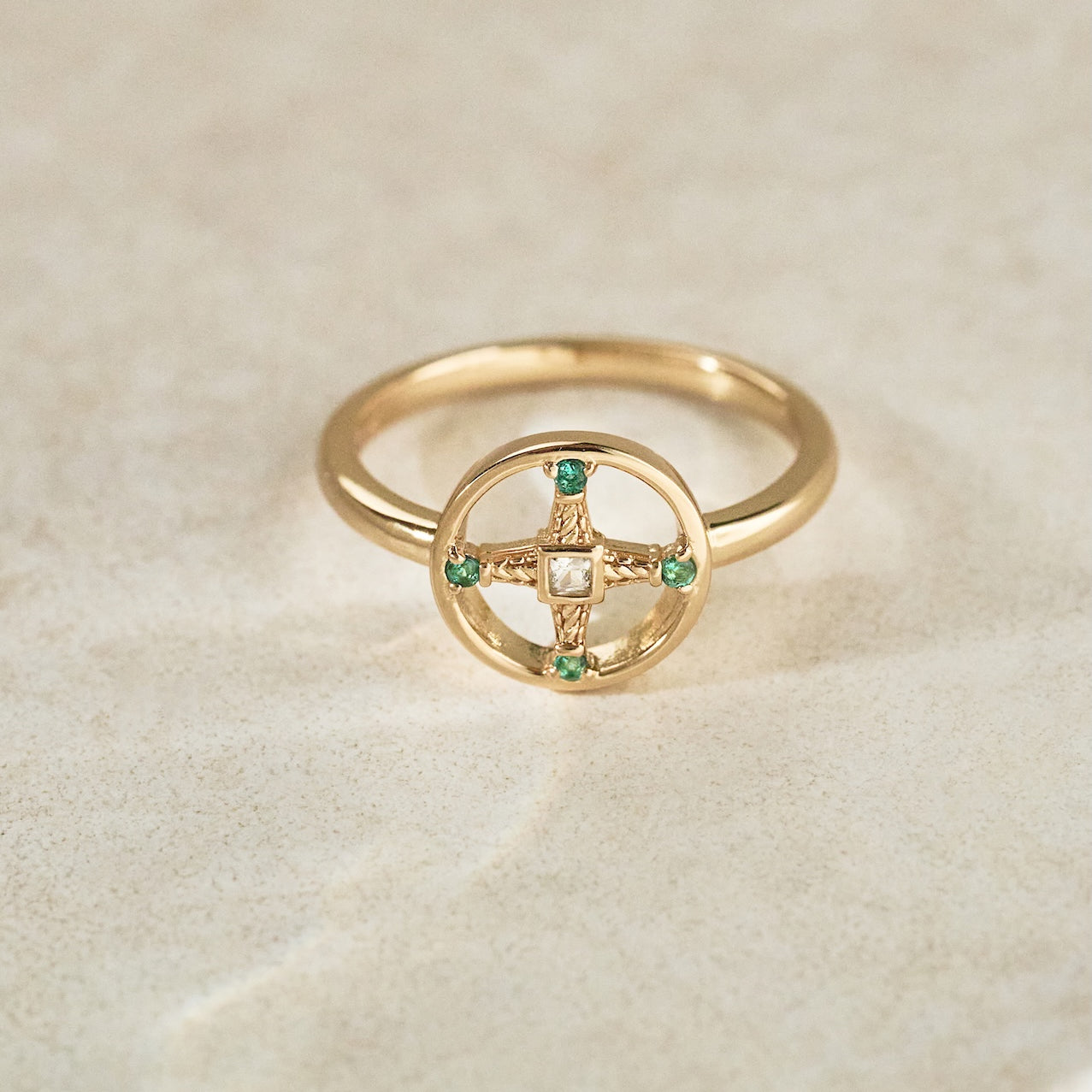 Gold ring with emerald stones on a beige background