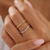 Close-up of a hand wearing two rings with colorful gemstones on a blurred background