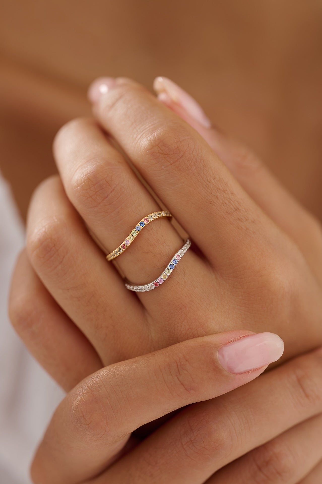 Close-up of a hand wearing two rings with colorful gemstones on a blurred background