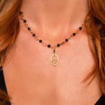 A close-up of a model wearing a delicate gold necklace with black and gold beads and a small gold pendant.
