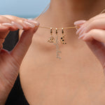 Close-up of a person holding a gold necklace with three charms: a triquetra symbol, a script ‘magickal’ charm, and a gold crescent moon with black and white stones.