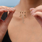 Close-up of a person holding a gold necklace with three charms: a triquetra symbol, a script ‘magickal’ charm, and a gold crescent moon with black and white stones.